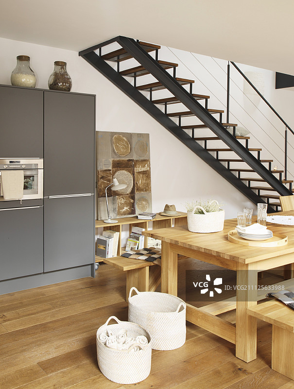 开放式厨房用餐区的实木家具，毗邻钢制楼梯图片素材