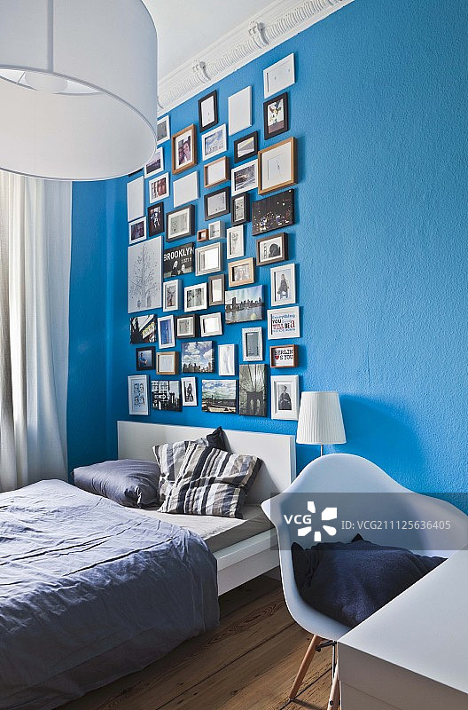 蓝色卧室墙上沙龙风格悬挂的各种相框照片图片素材