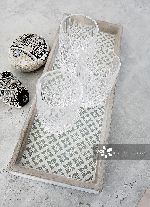 彩绘鹅卵石旁边的图案混凝土托盘上的三个水晶玻璃杯图片素材