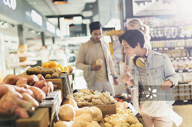 戴着耳机在市场上购买农产品的年轻女子图片素材