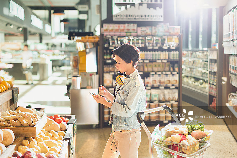 戴着耳机在市场购物的年轻女人图片素材
