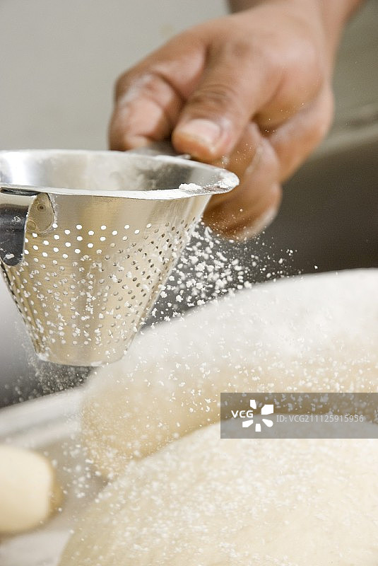 用筛子给未烤的面包撒面粉图片素材