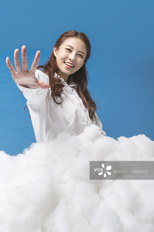 女人坐在云朵状棉球上伸出手臂图片素材