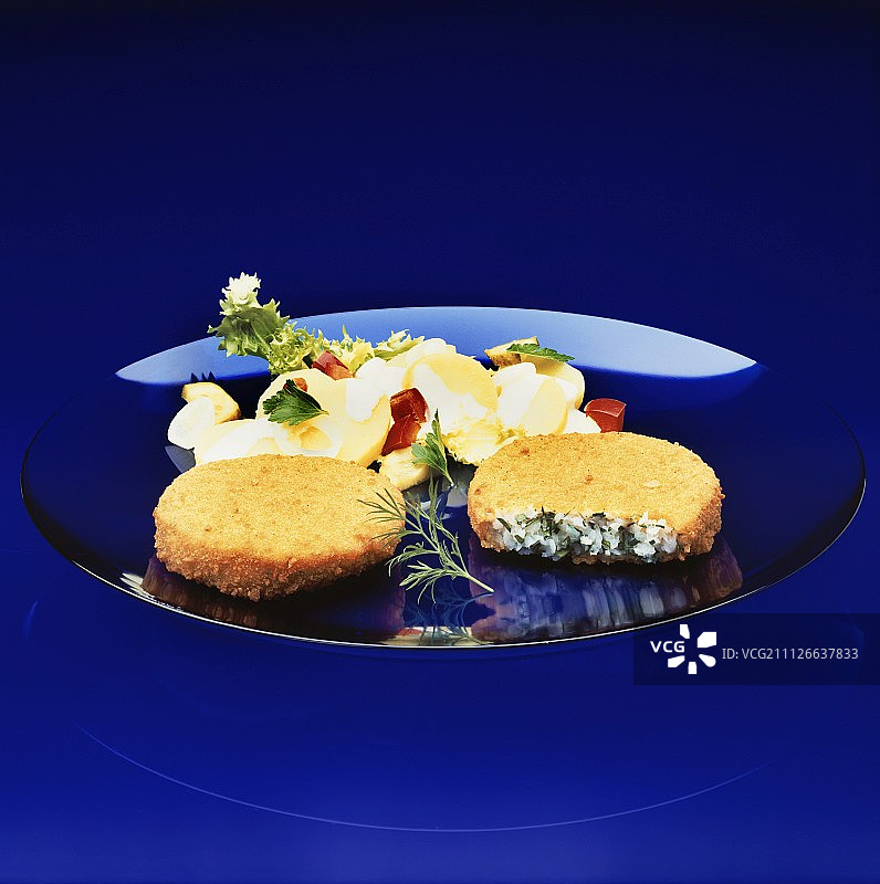 蓝色盘子里的两块面包炸鱼饼和土豆沙拉图片素材