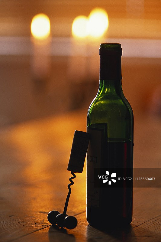 靠在红酒瓶上的开瓶器与燃烧的蜡烛图片素材