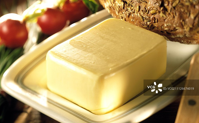 黄油碟中的黄油，后面是面包和萝卜图片素材