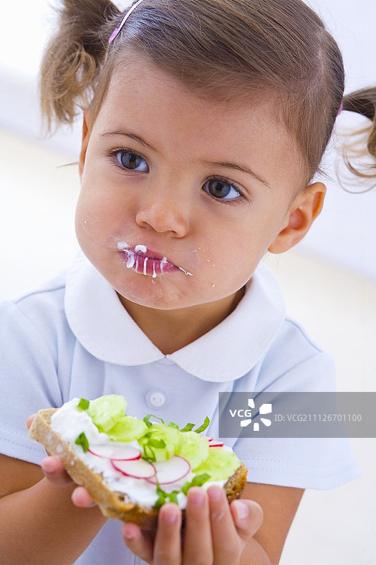 小女孩吃面包片，配凝乳、黄瓜和萝卜图片素材