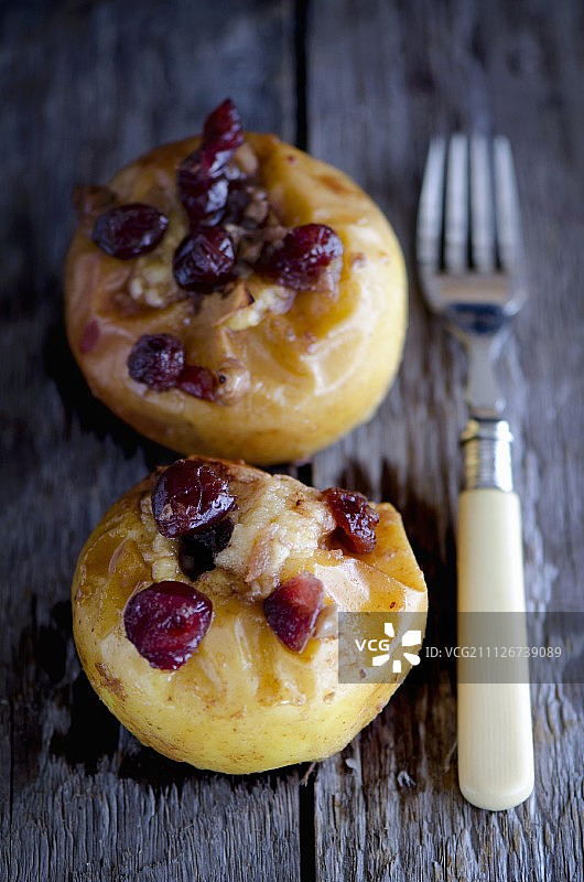 两个带蔓越莓的烤苹果，放在带叉子的木桌上图片素材