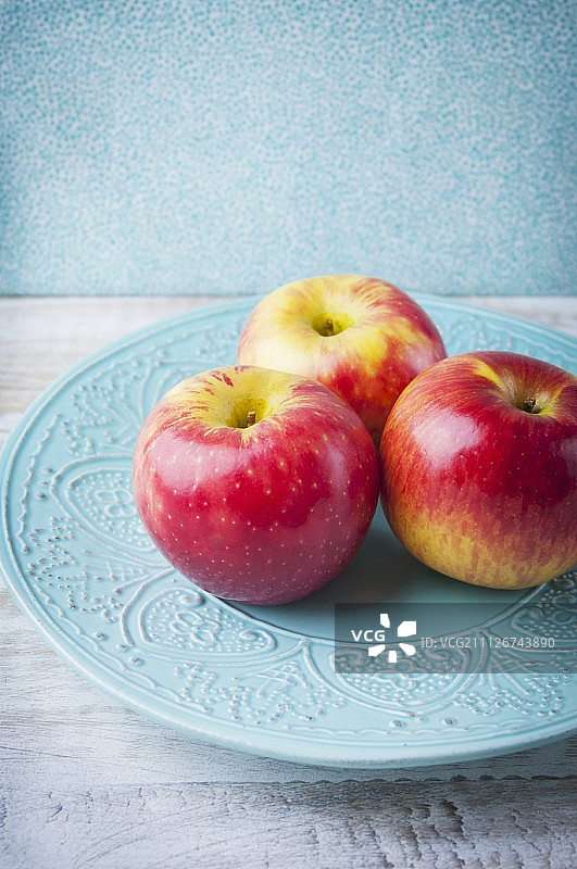 蓝色陶瓷盘上的三个粉红佳人苹果图片素材
