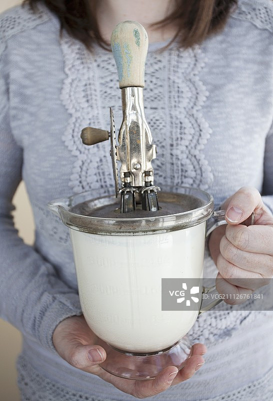 一位女士拿着量杯奶油和一个旧式手动搅拌器图片素材
