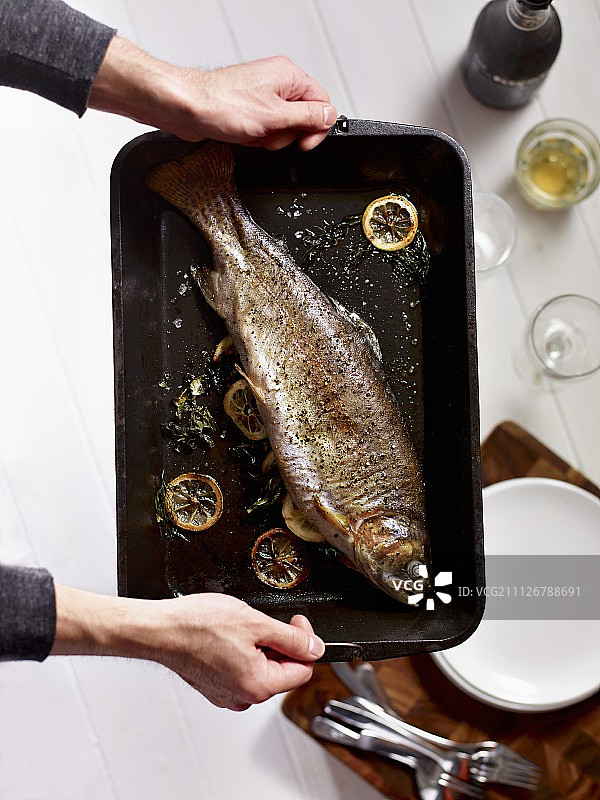 手拿烤盘里的烤鳟鱼图片素材