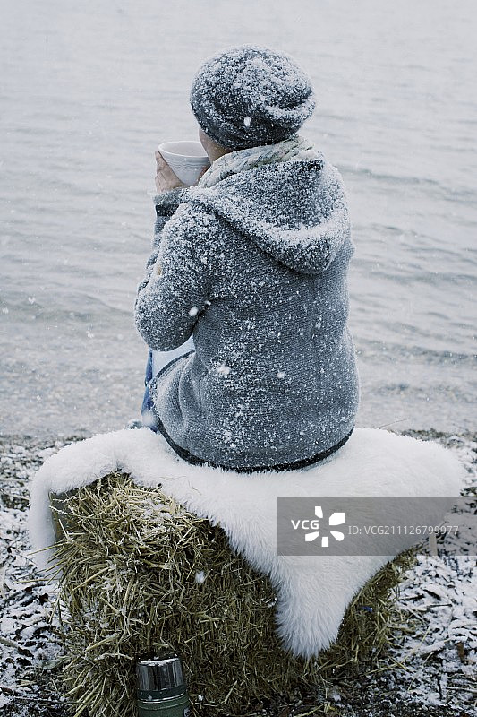 一位女士坐在雪中的河岸边喝茶图片素材