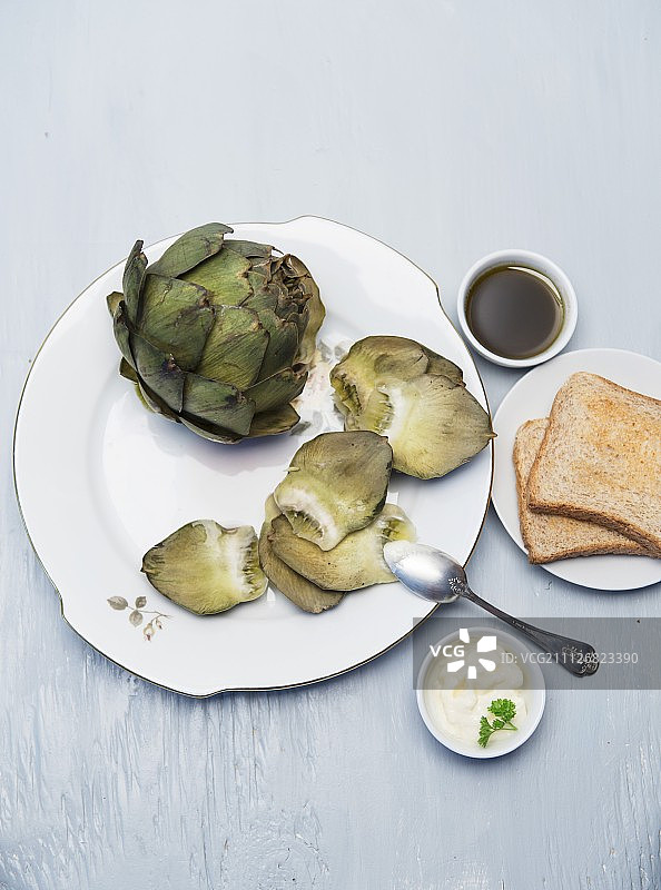 瓷盘上的煮熟的朝鲜蓟配蒜泥蛋黄酱和油醋汁图片素材
