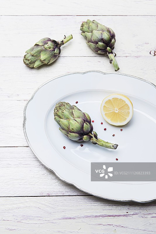 瓷盘上的新鲜小朝鲜蓟柠檬和粉红胡椒图片素材