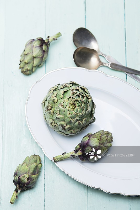 一个新鲜的朝鲜蓟和在瓷盘上的小朝鲜蓟图片素材