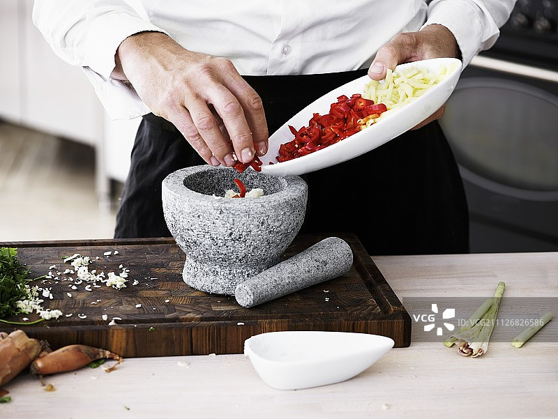 男人将辣椒和柠檬草放入石臼中捣碎图片素材