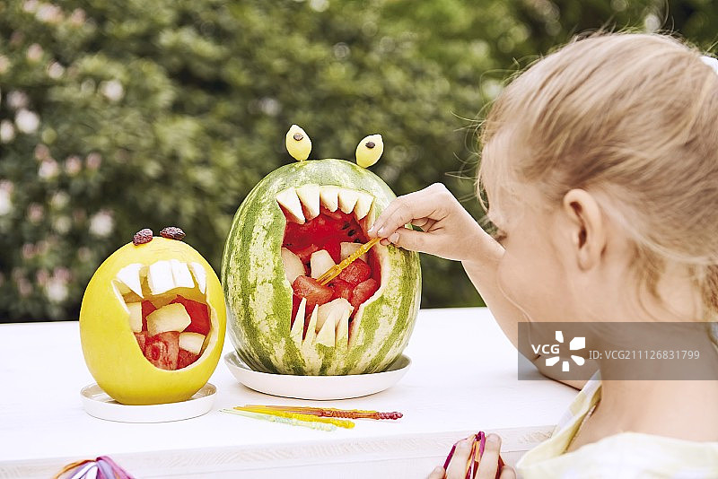 掏空的瓜壳中盛放的瓜丁，一个小女孩用棍子取一块图片素材