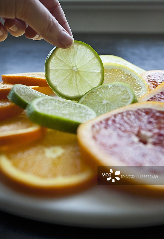 女人从装满柑橘水果片的托盘中取一片酸橙图片素材