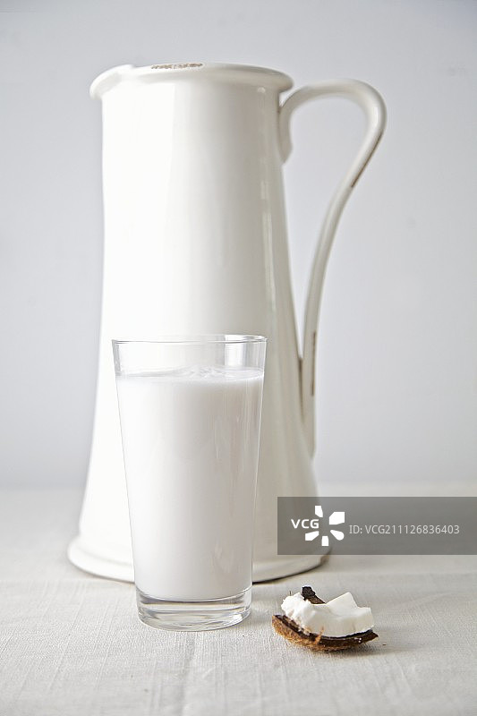 玻璃杯中的椰奶和后面的白色水罐图片素材