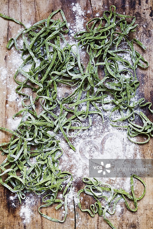 撒有面粉的木质表面上的自制绿色意大利细面条图片素材