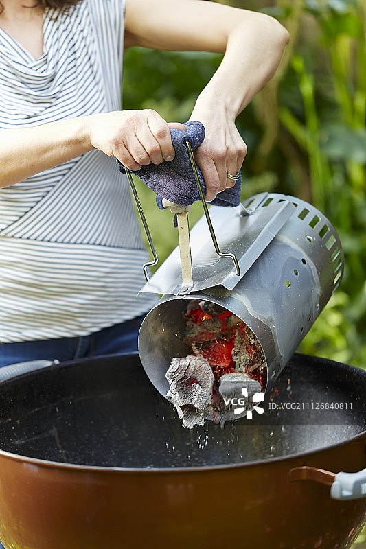 女人将点燃的木炭从引燃器倒入烤炉图片素材