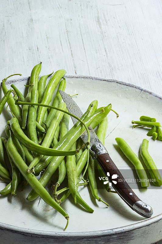 白色盘子上准备用刀切的新鲜豆类图片素材