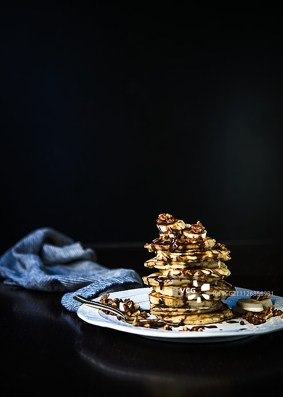 堆叠的香蕉煎饼，配有烤山核桃、香蕉片和榛果巧克力酱图片素材