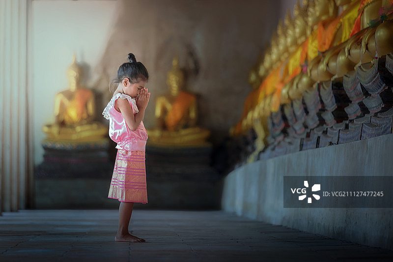 身穿泰国传统佛教服装的亚洲儿童，虔诚地朝拜佛像图片素材