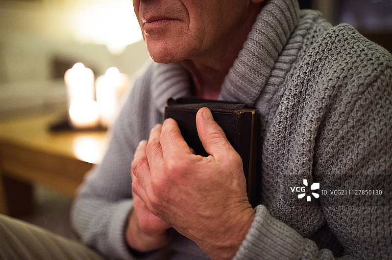 年长的男人手持圣经祈祷，身后点燃蜡烛图片素材