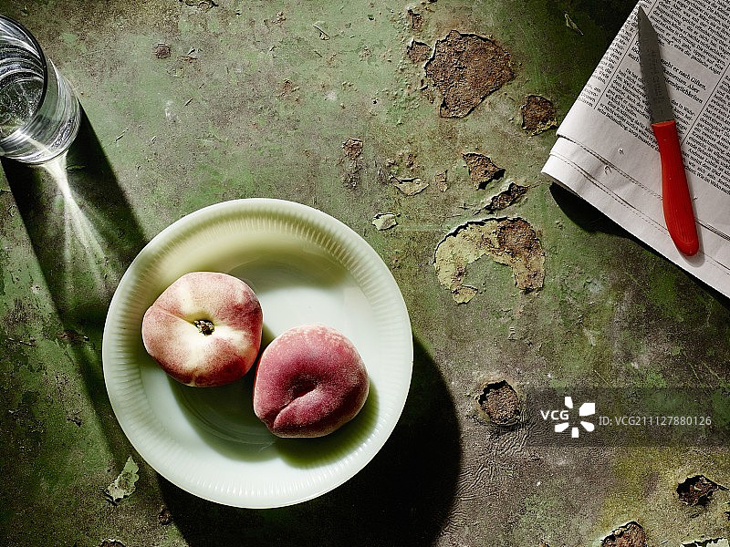 报纸和水果刀旁的盘子里放着桃子图片素材