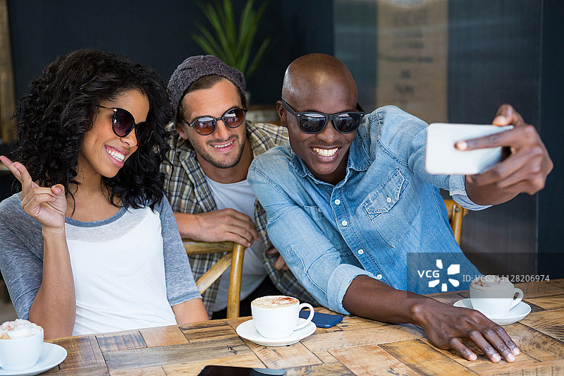 在咖啡店里戴着太阳镜自拍的快乐的多种族朋友们图片素材