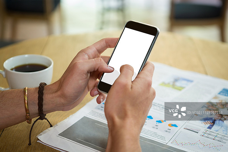 在咖啡店里，男人在桌旁使用手机的裁剪图图片素材