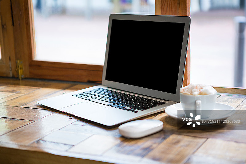 咖啡馆桌子上咖啡杯旁的笔记本电脑特写图片素材