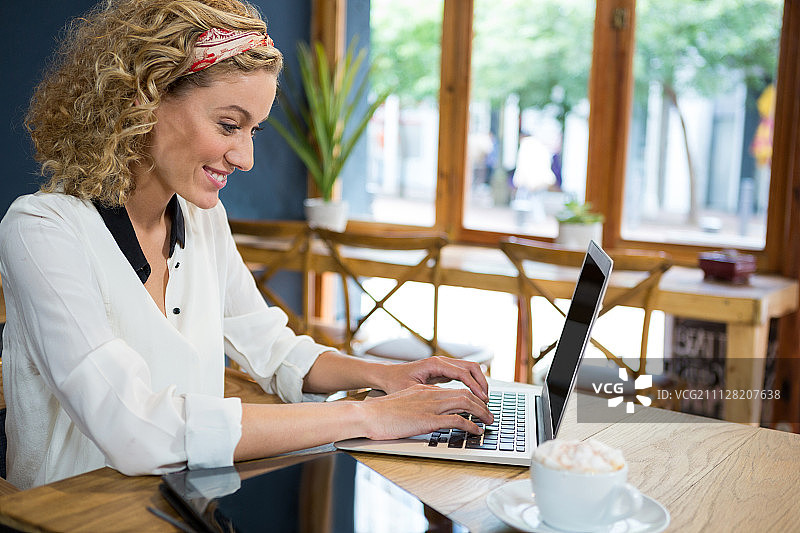 在咖啡馆桌旁使用笔记本电脑的年轻微笑女人图片素材