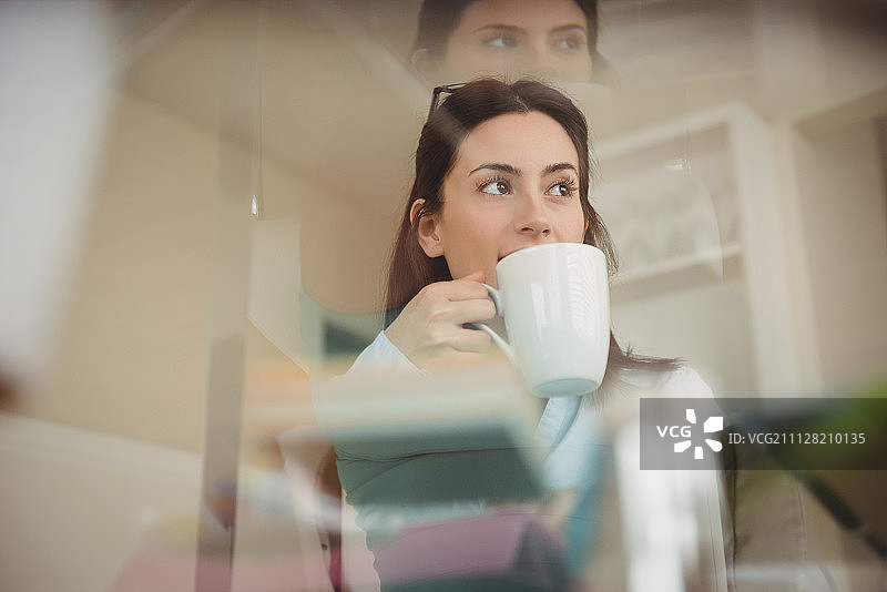 在家中玻璃桌旁喝咖啡的女人图片素材