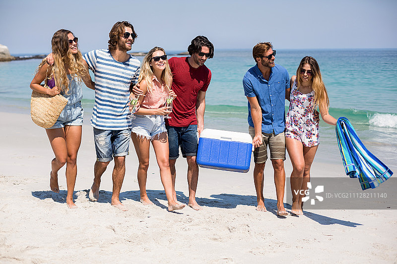 阳光明媚的日子里，在海滩上行走的朋友们全身像图片素材