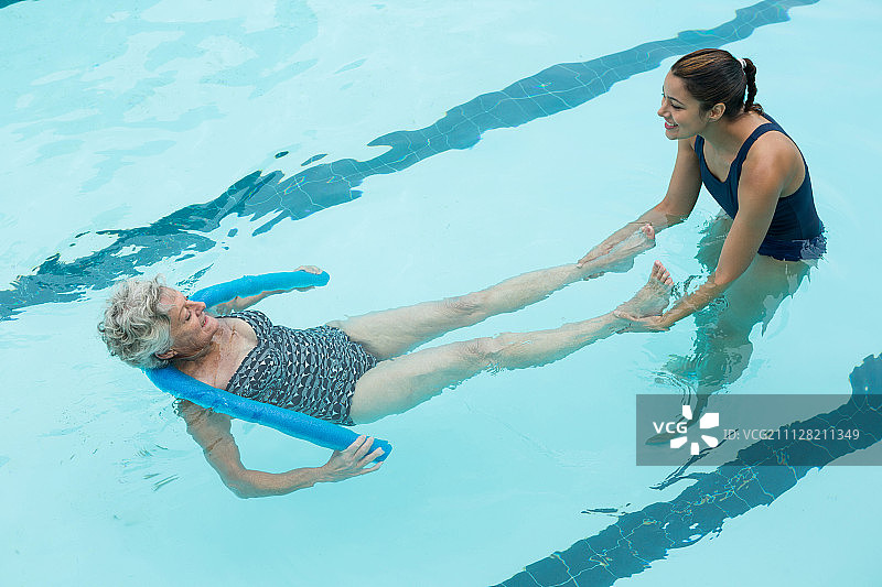 提升的观点，微笑的女教练帮助年长妇女在游泳池图片素材