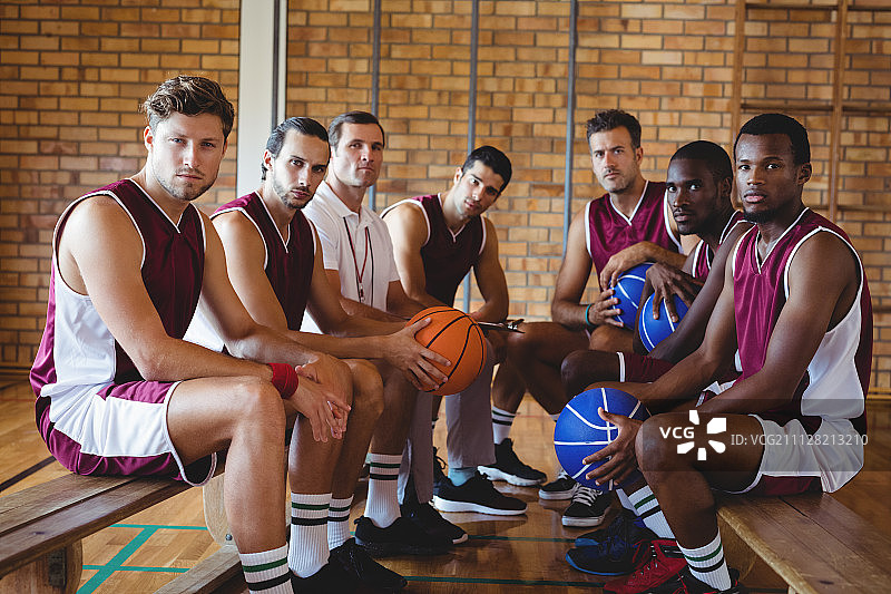 自信的教练和篮球运动员坐在球场长椅上的肖像图片素材