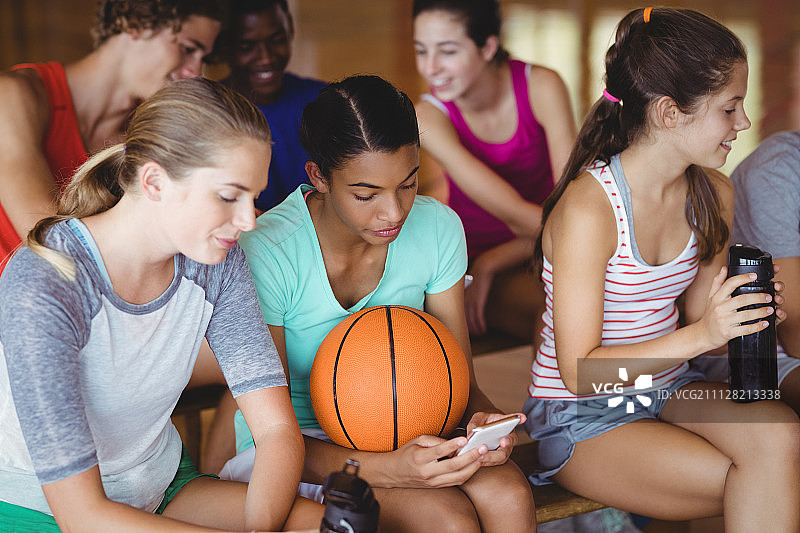 在篮球场放松时使用手机的微笑高中生图片素材