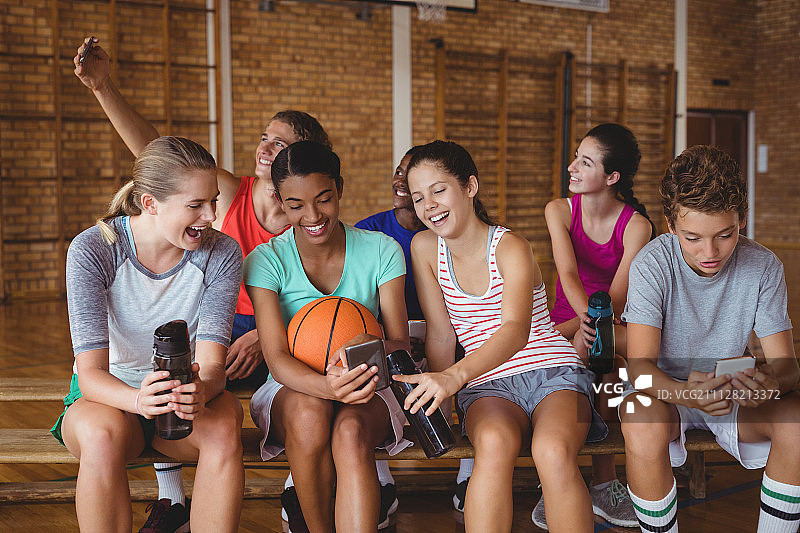 在篮球场放松时使用手机的微笑高中生图片素材