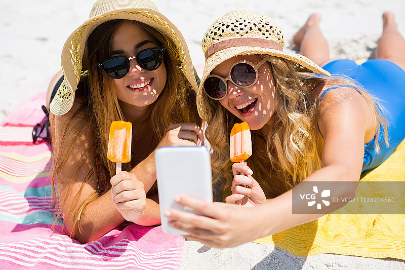 在海滩上吃冰棒时自拍的微笑女性朋友图片素材