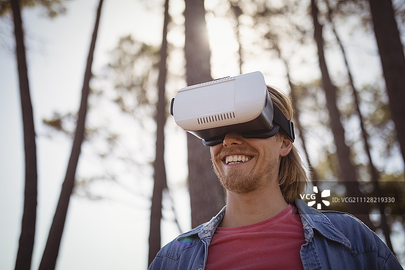 站在森林中佩戴VR虚拟现实模拟器的微笑年轻人图片素材