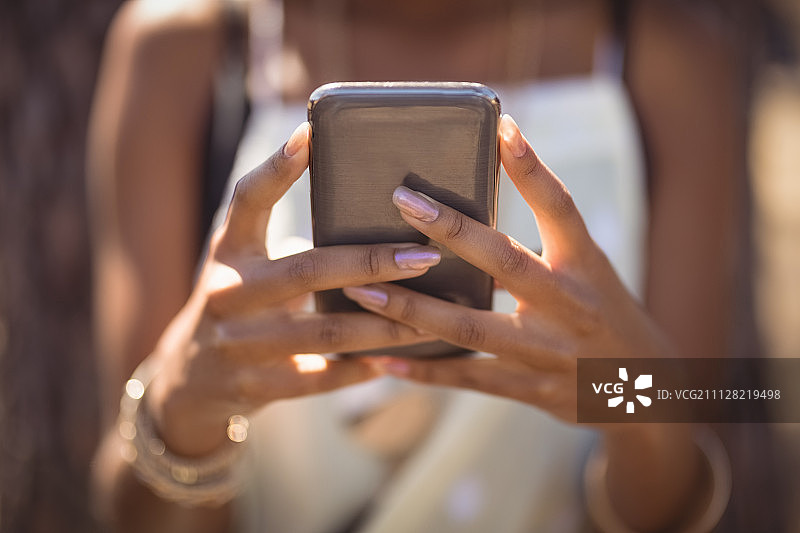女子靠在树旁使用智能手机的半身照图片素材