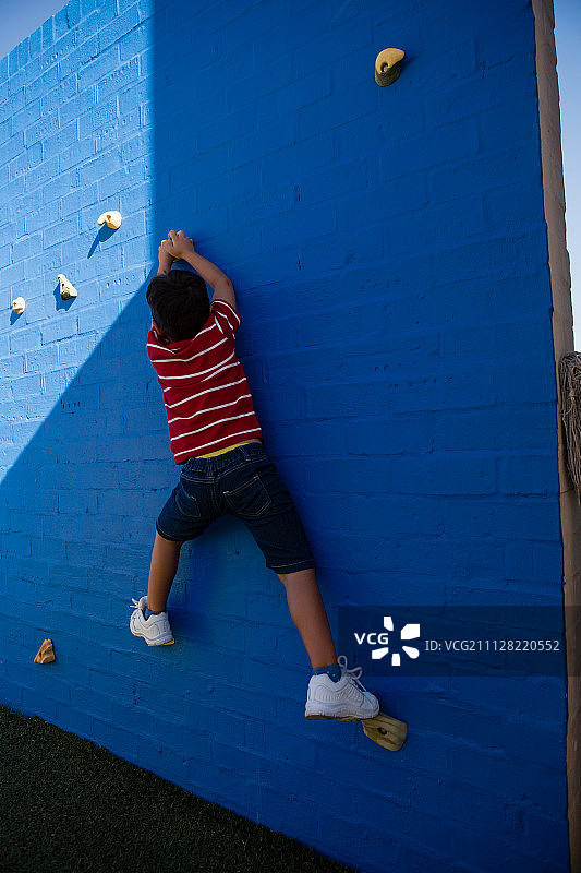 男孩在学校操场攀爬蓝色墙壁背影图片素材