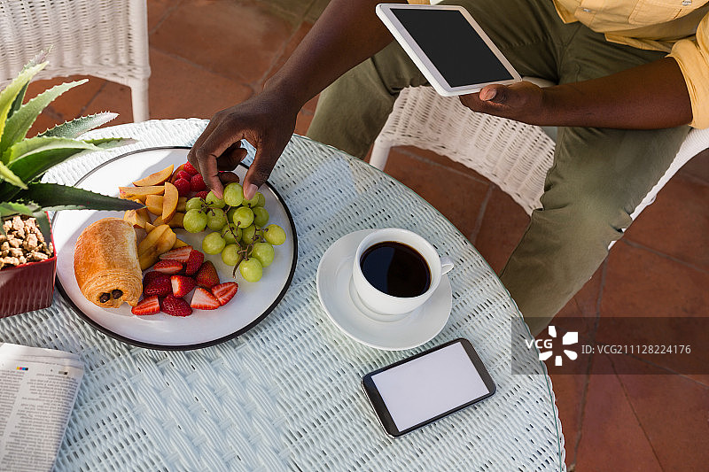男人在咖啡馆使用平板电脑吃葡萄的腰部特写图片素材