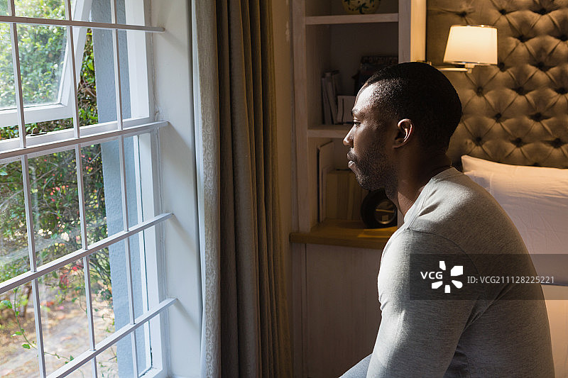 男子在家中窗边坐在床上的侧视图图片素材
