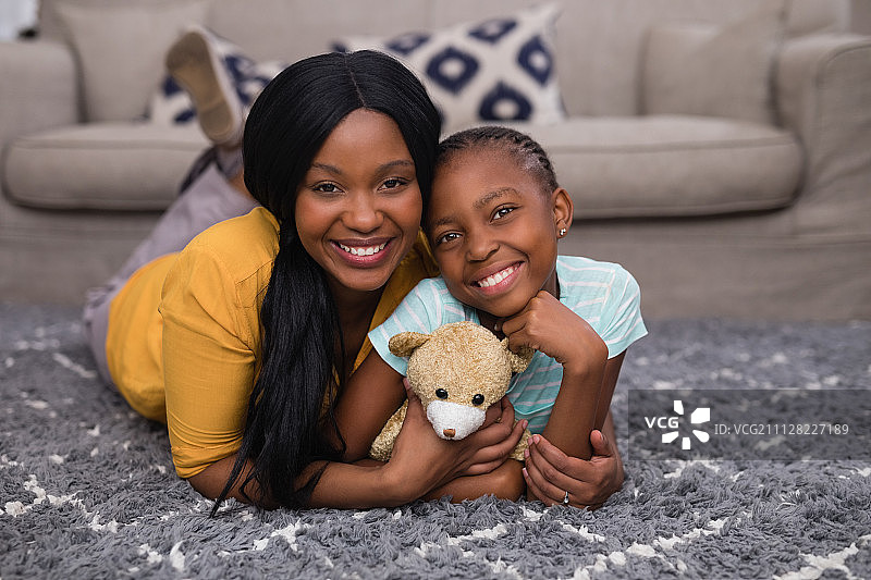 母亲和女儿抱着泰迪熊躺在家里的地毯上图片素材