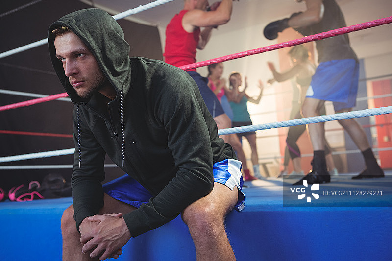 年轻男拳击手坐在拳击台上，运动员在健身室训练图片素材