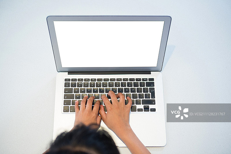 女孩在厨房台面上用笔记本电脑打字的高角度视图图片素材