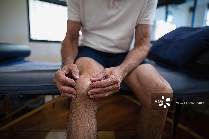 老年男性患者在医院病房里痛苦地按着膝盖，腹部中段图片素材